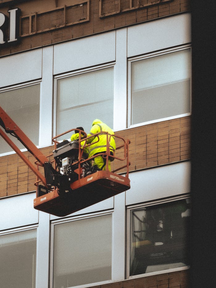 Two workers on a cherry picker doing maintenance on a building façade.